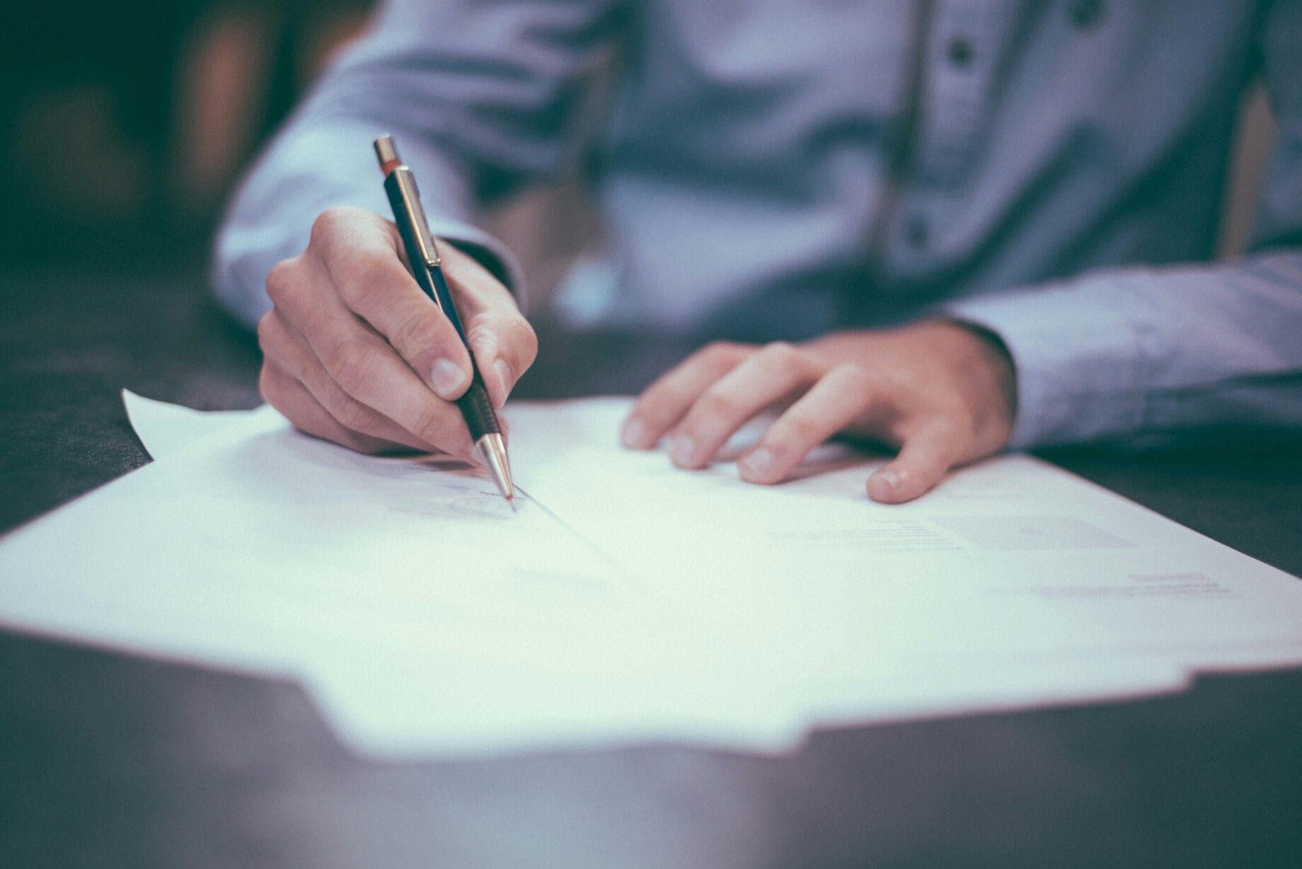 Persona in camicia che compila un documento con la penna su una scrivania
